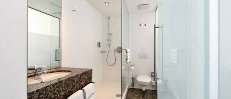 Un baño moderno con lavamanos de granito, cabina de ducha de vidrio y inodoro blanco.
