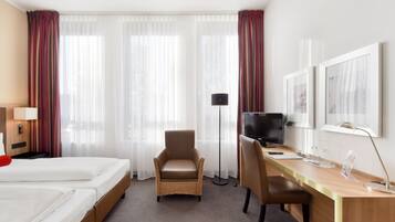 Habitación de hotel con dos camas, un escritorio, una silla, un televisor y una lámpara de pie.
