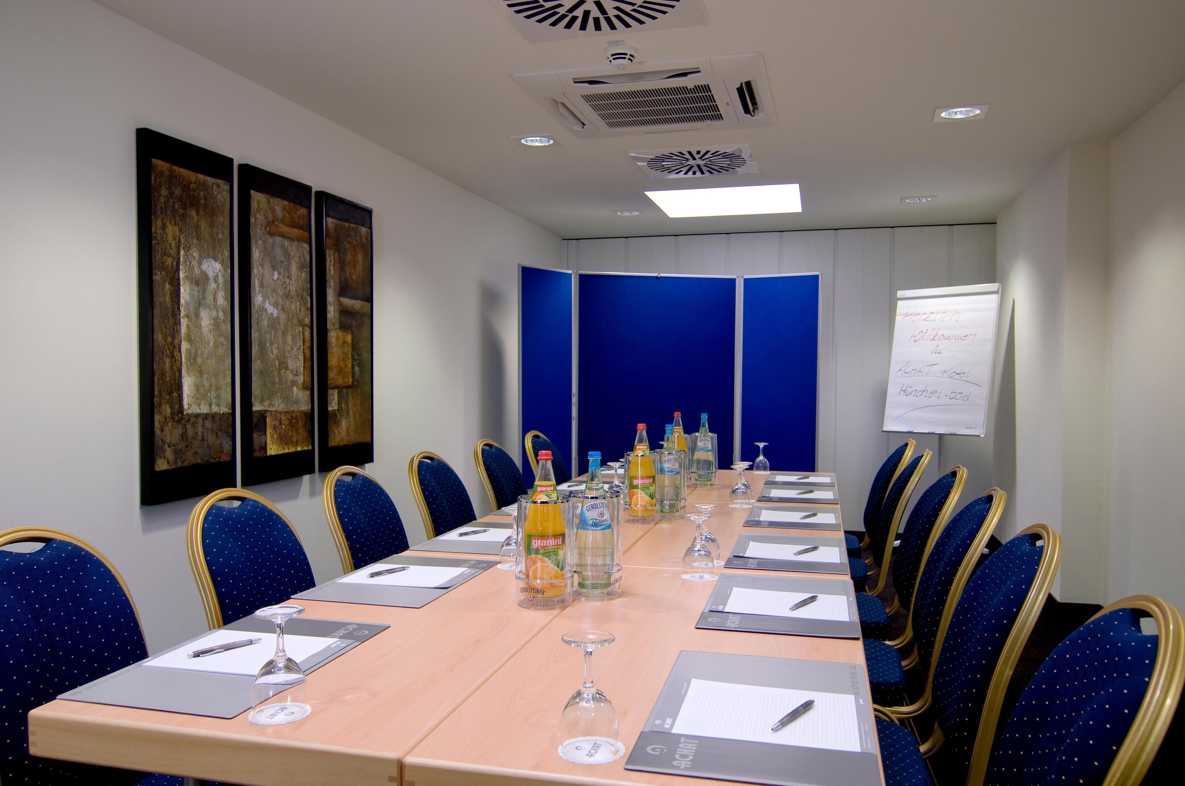 Ein Konferenzraum mit einem langen Tisch, blauen Stühlen und einer Whiteboard-Tafel.