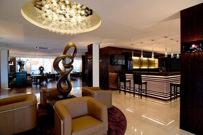 A modern lobby with a central bar area, seating arrangements, and a distinctive spiral sculpture. - ACHAT Hotel München Süd (Munich)