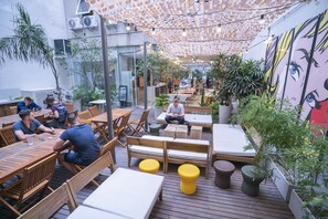 An outdoor seating area with wooden tables and benches, surrounded by potted plants and a ceiling with a unique pattern. - America del Sur Hostel Buenos Aires (Buenos Aires)