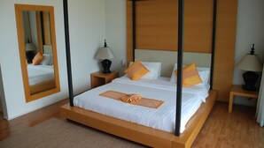 A four-poster bed with white linens and orange accents, a wooden nightstand with a lamp, and a mirror on the wall. - The Park Samui (Koh Samui)