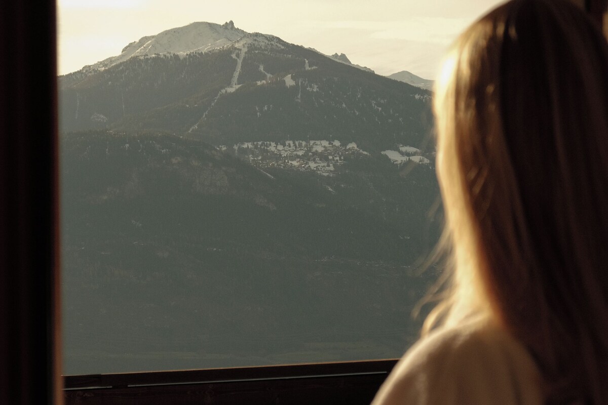 Una persona sentada junto a una ventana con vistas a la montaña.