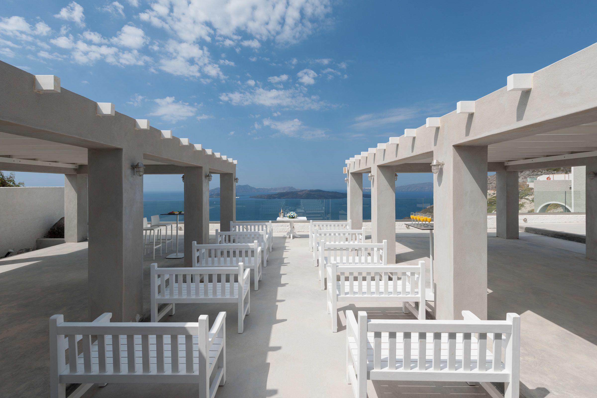 A beachside outdoor seating area with white benches arranged in rows, overlooking the sea.
