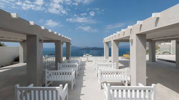 A beachside outdoor seating area with white benches arranged in rows, overlooking the sea.