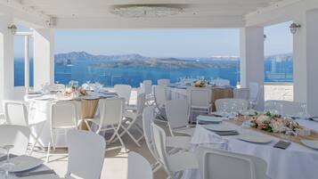 Un restaurante con mesas y sillas blancas, con vistas panorámicas al mar y a las montañas.
