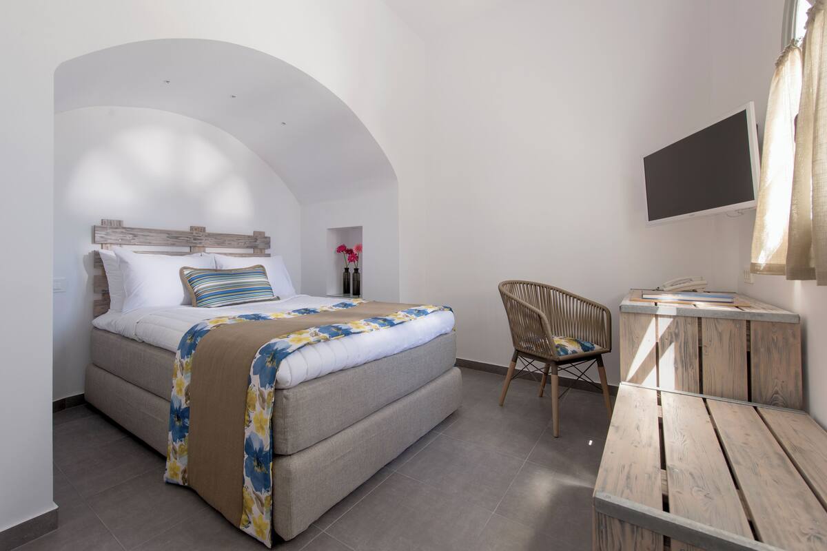 A bedroom with a bed, a chair, a desk, and a TV.