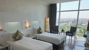Habitación de hotel con dos camas, una mesita con frutero, una silla y un ventanal con vista a la ciudad.