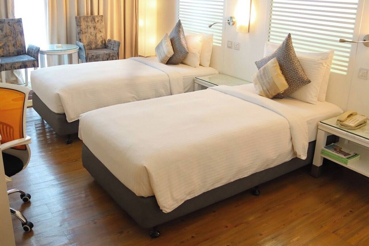 A hotel room with two beds, a small table, a chair, and a lamp.