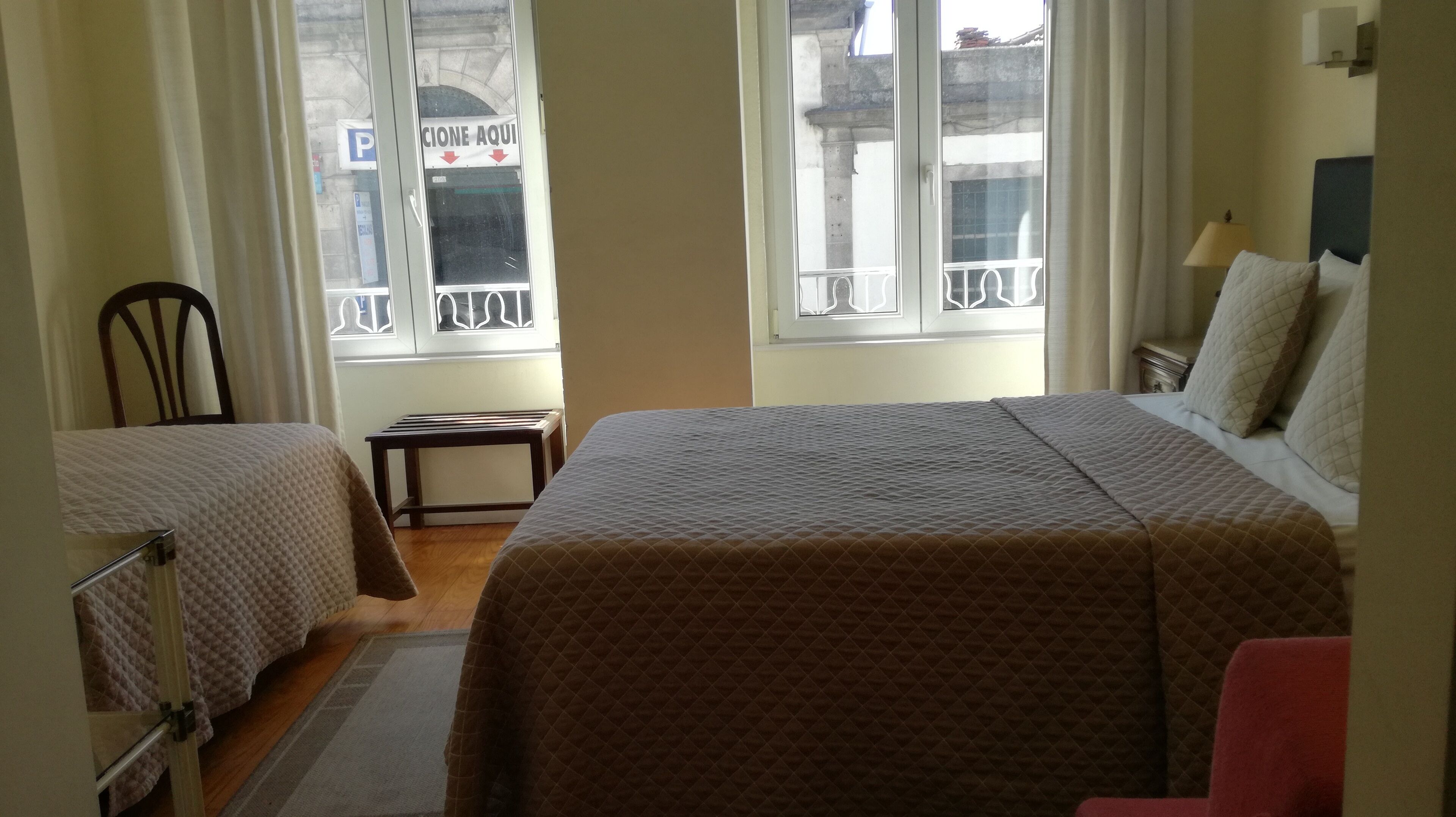 Hotellihuone, jossa on kaksi sänkyä, pieni pöytä ja ikkuna, josta on näkymä kadulle.