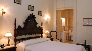 A neatly made bed with a wooden headboard, two bedside lamps, and a nightstand with a lamp. A chair and a small table with a lamp are also visible. - Hotel Miradaire Porto (Porto)
