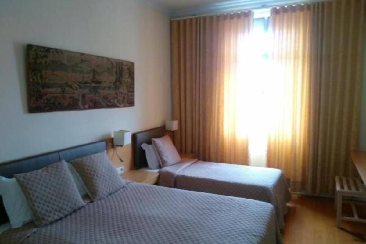 A hotel room with two beds, a painting on the wall, and a window with curtains.