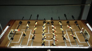 A foosball table with a wooden frame and metal rods, featuring a soccer field layout with goal areas and player figures. - Hotel Restaurant Linde (Otterstadt)