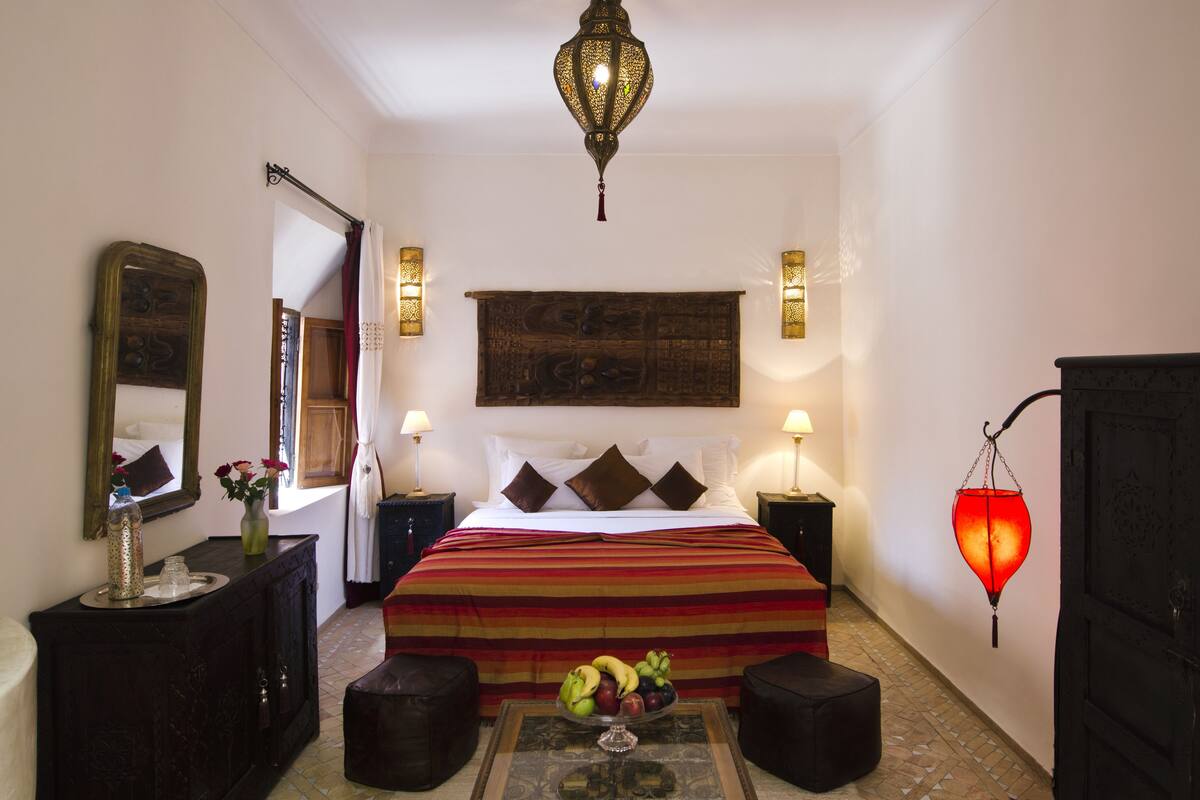 A bedroom with a large bed, a nightstand, a dresser, a mirror, a wall-mounted lamp, and a hanging lantern.