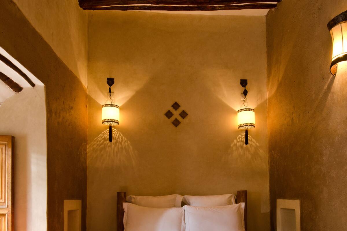 A traditional Moroccan room with a bed, wooden beams, and a tray with a teapot and glasses.