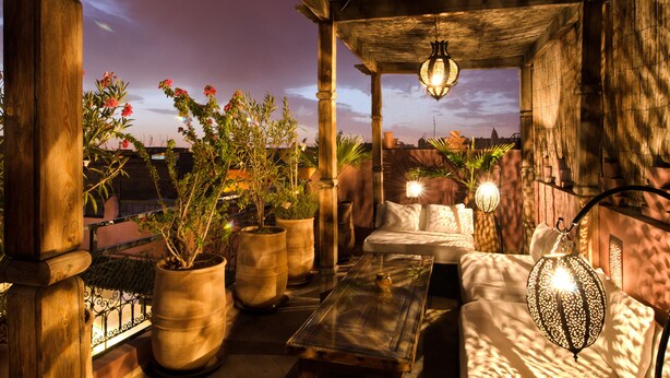 A cozy outdoor seating area with a wooden table, cushioned seating, and potted plants.