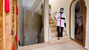 A person standing on a staircase in a hallway with a wooden door and a mirror on the wall.