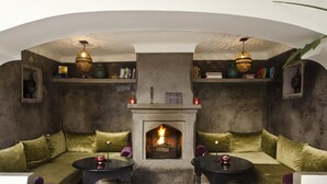 A cozy lounge area with a fireplace, green velvet sofas, and two small tables with candles.