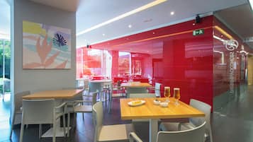 A modern restaurant with white chairs and tables, red accents, and a large abstract painting on the wall.