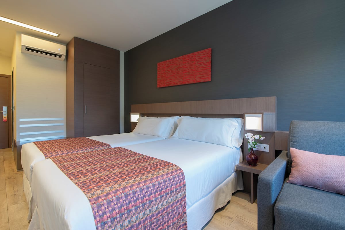 A hotel room with a large bed, a bedside table with a vase of flowers, and a red abstract painting on the wall.