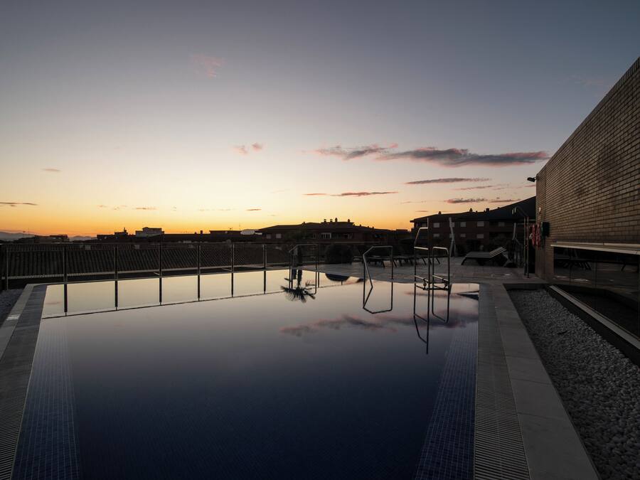 Piscina exterior com vista clara para o pôr do sol e edifícios circundantes.