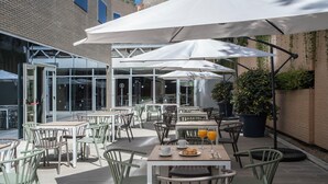 Un café en plein air avec des tables et des chaises, des parasols, et un bâtiment en briques en arrière-plan.