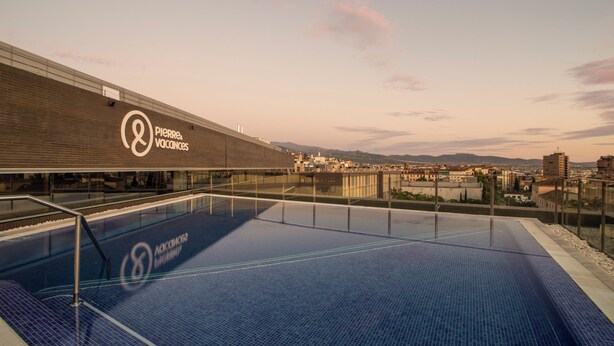 Une piscine sur le toit offrant une vue sur le paysage urbain et les montagnes au loin.