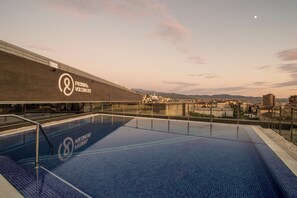 Ein Pool auf dem Dach mit Blick auf eine Stadtlandschaft und entfernte Berge.
