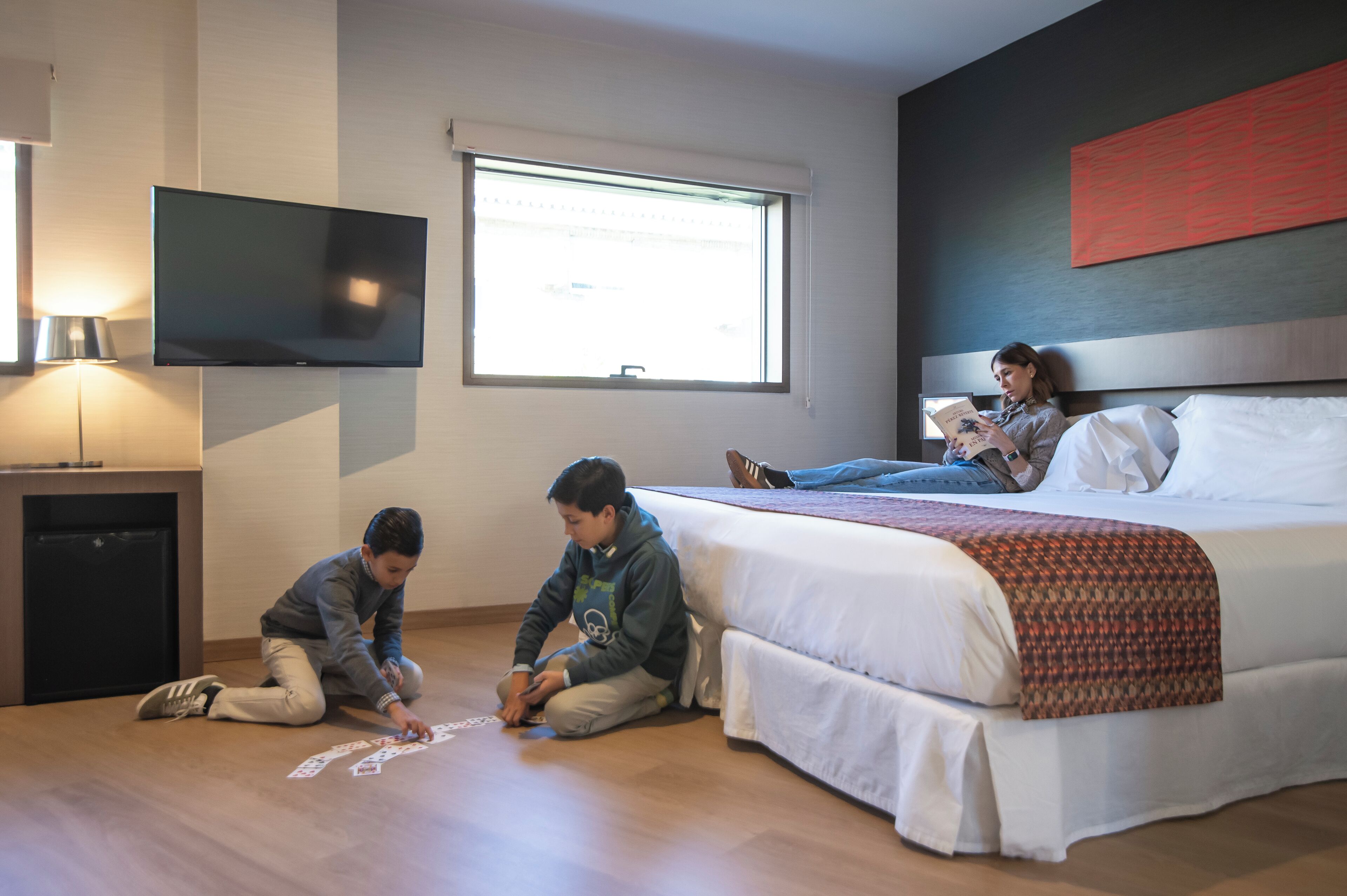 A hotel room with a bed, a TV mounted on the wall, and a window.