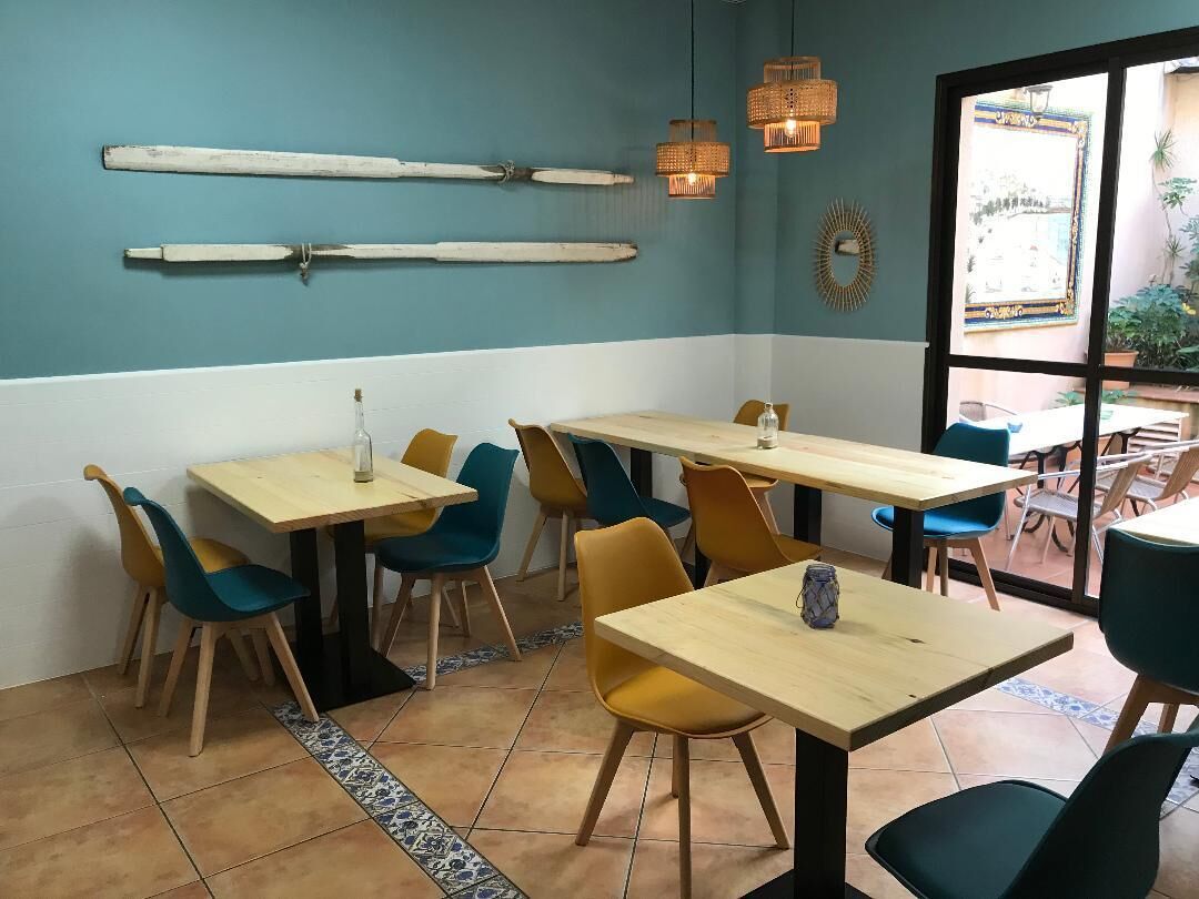 Ein Restaurantinneres mit Holztischen und -stühlen, einer blauen und weißen Farbgestaltung und Blick durch eine Glastür.