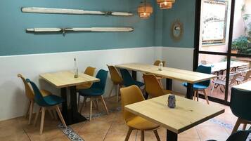 A restaurant interior with wooden tables and chairs, a blue and white color scheme, and a view through a glass door.