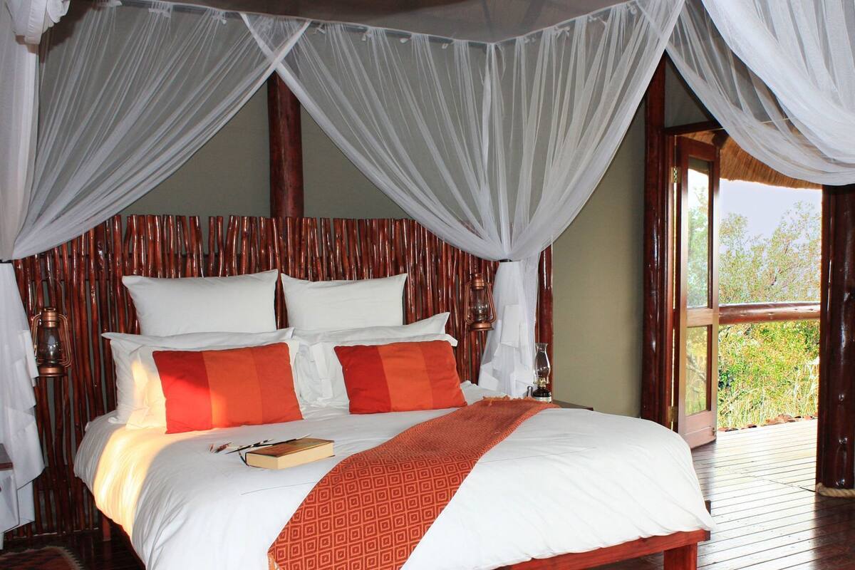 A bed with white and orange bedding, a wooden headboard, and a canopy.