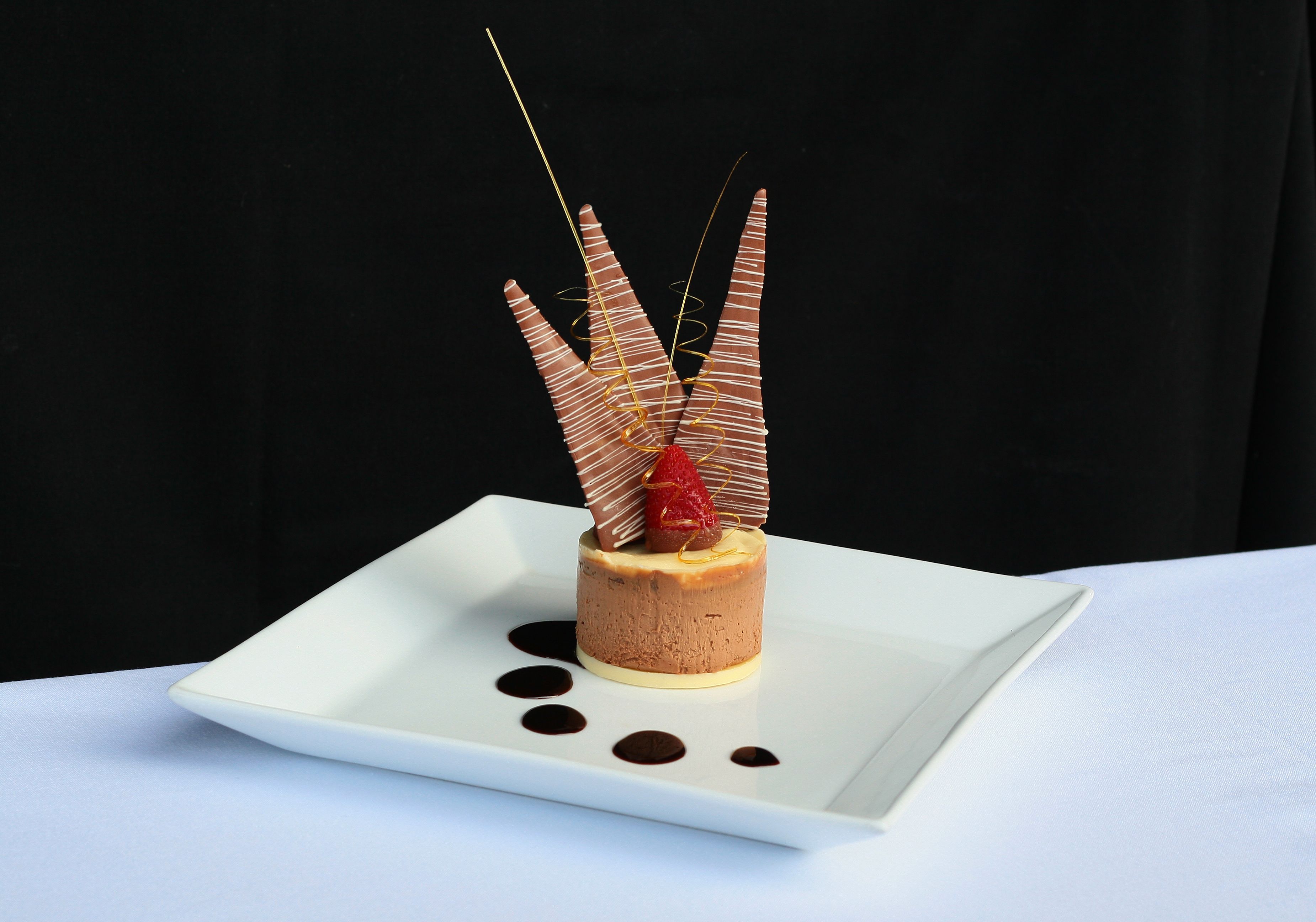 A dessert on a white square plate with chocolate and strawberry decorations.