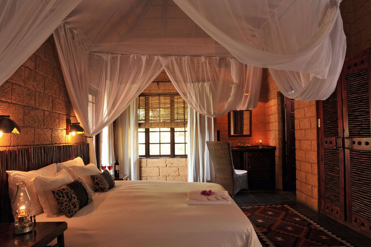A bedroom with a large bed, white canopy, and a brick wall.