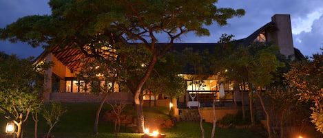 A modern house with a stone facade, large windows, and a well-maintained garden with trees and a pathway.
