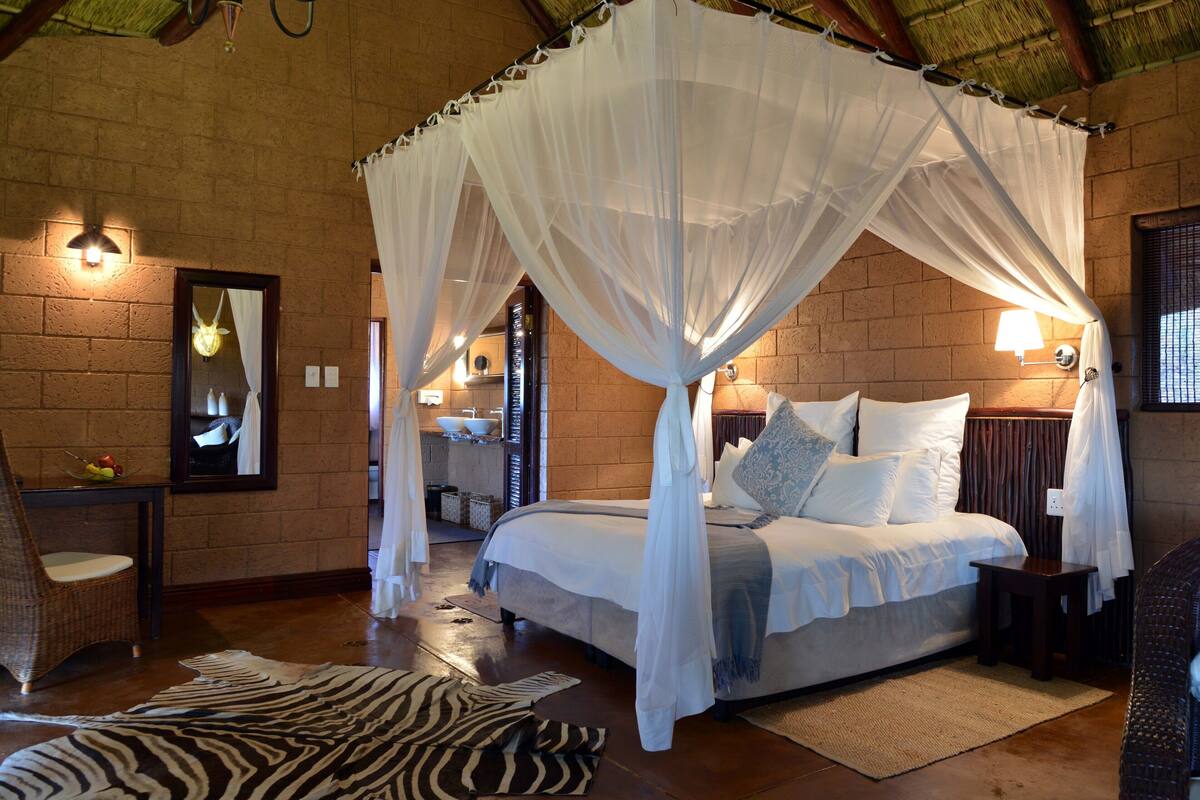 A room with a four-poster bed, a zebra rug, a wicker chair, and a mirror on the wall.