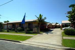 Un hotel con fachada roja y amarilla, una bandera azul y una palmera en primer plano.
