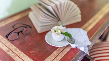 Una mesa de madera con un par de gafas, un libro doblado, una taza blanca pequeña con una flor y una cuchara.