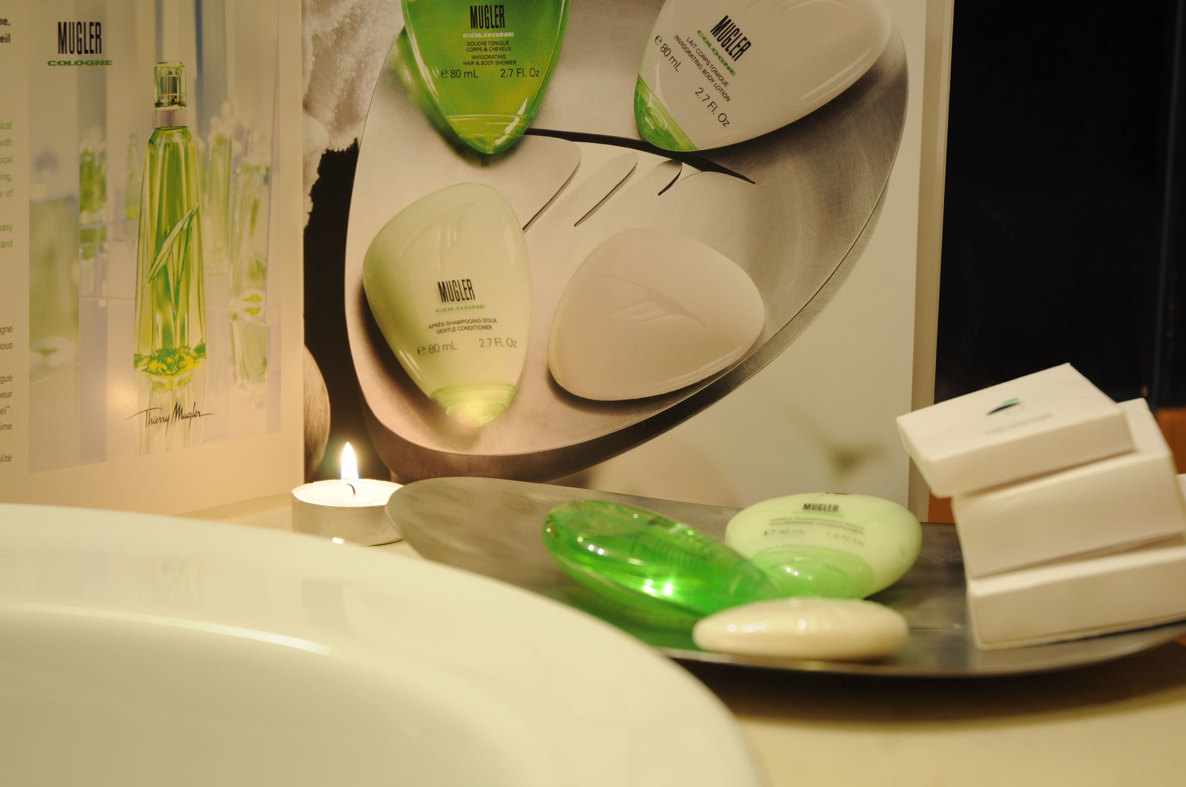 Une salle de bain équipée d’un lavabo, d’un miroir et de produits de toilette, notamment un flacon vert, un flacon blanc et un savon blanc.
