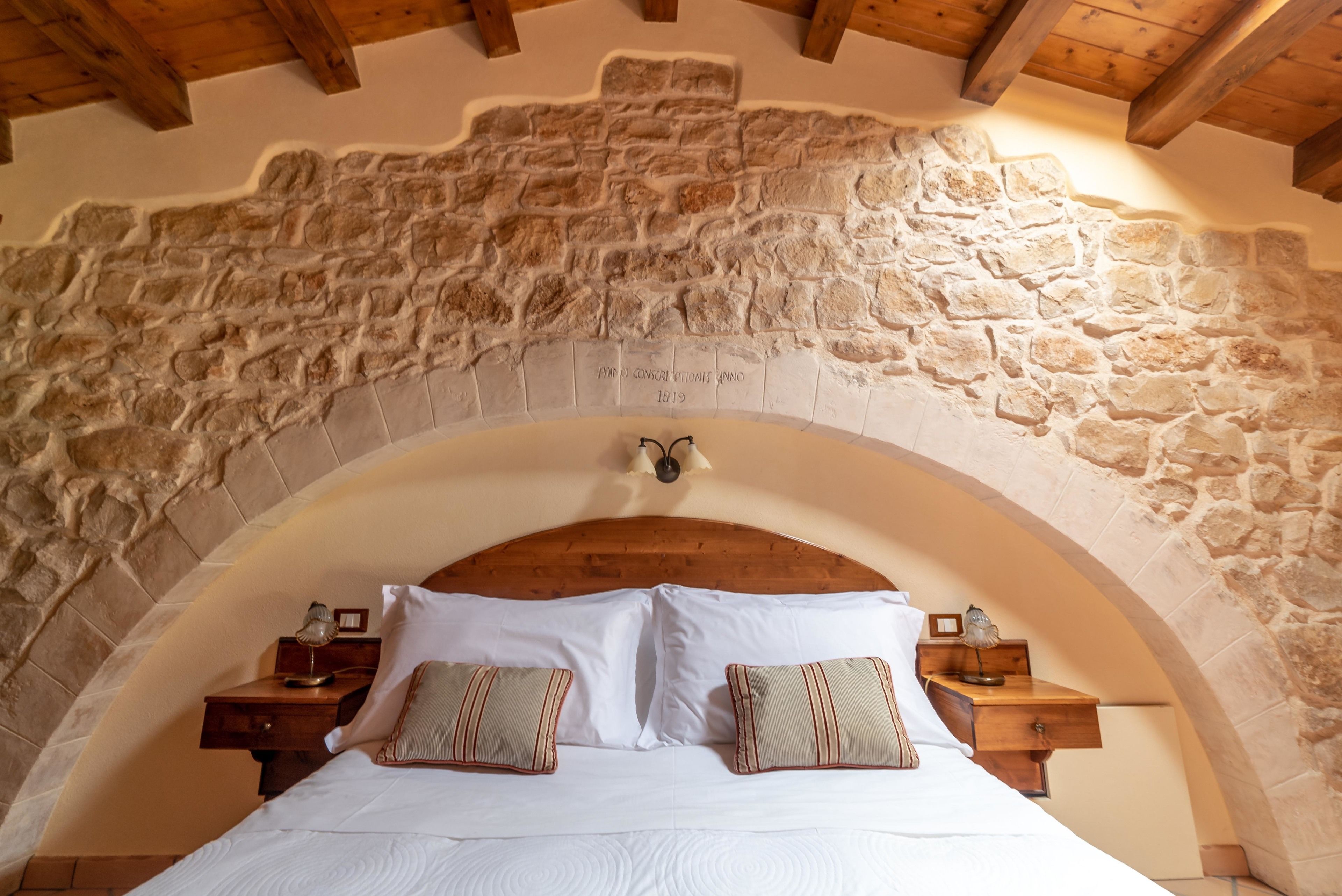 Un dormitorio con techo abovedado de piedra, cabecera de madera y dos mesitas de noche con lámparas.