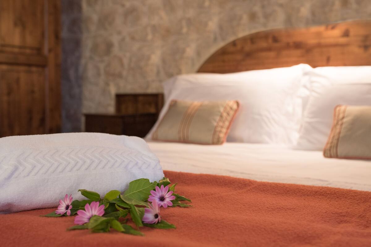 A neatly made bed with white linens and a pink flower arrangement on a brown blanket.