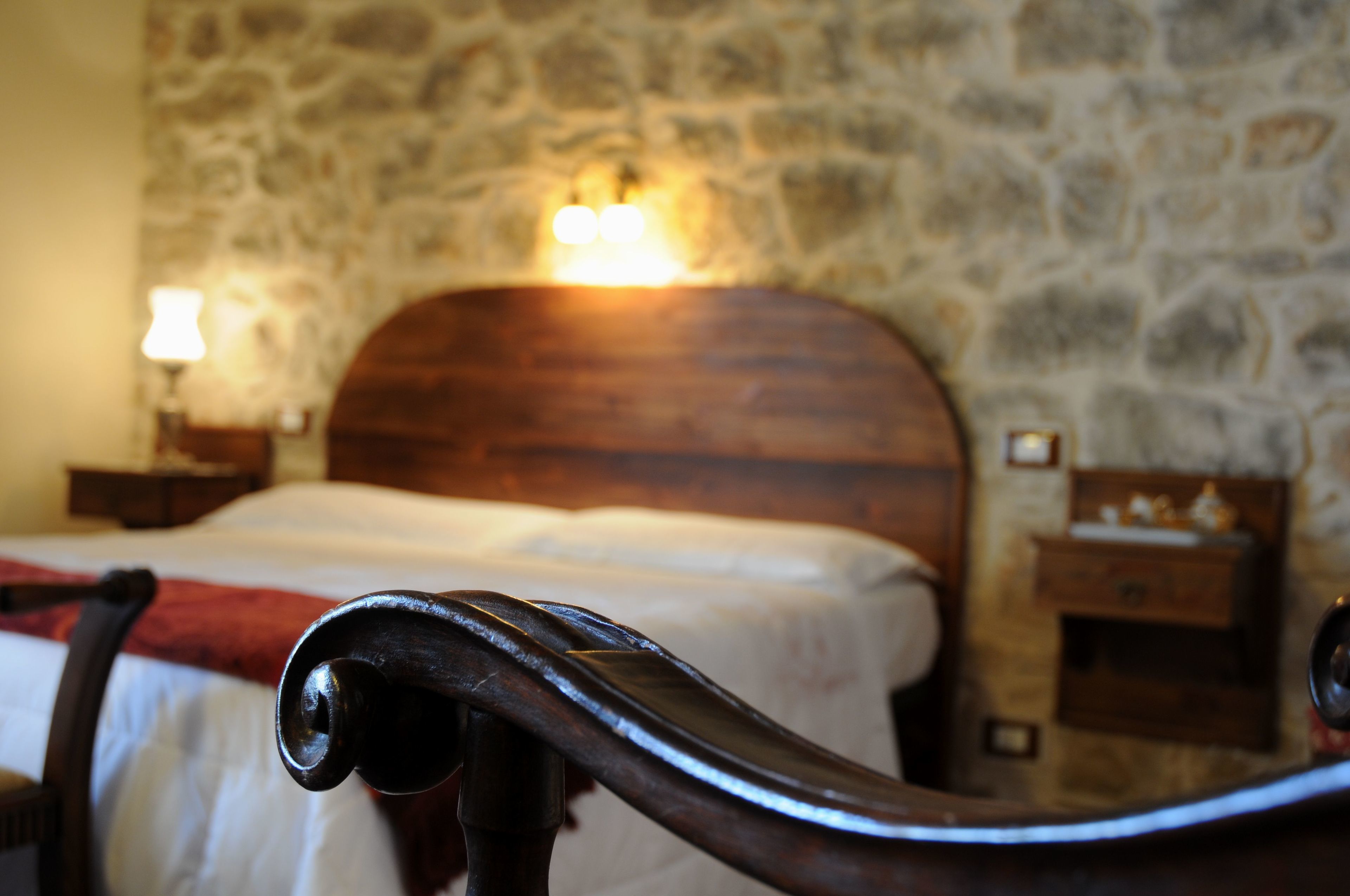 Ein Bett mit Holz-Kopfteil, ein Nachttisch mit Lampe und eine Steinsäule im Hintergrund.