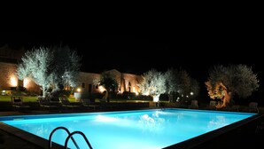 A swimming pool at night with surrounding trees and a building in the background. - Torre Don Virgilio Country Hotel (Modica)