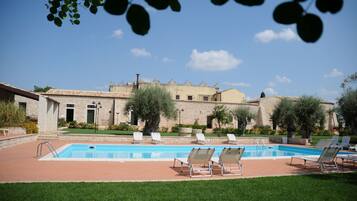 Relax by the serene pool surrounded by lush greenery and a traditional stone building.