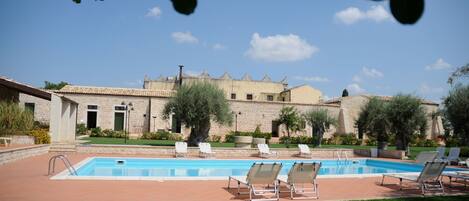 A swimming pool with lounge chairs, a stone building, and a clear sky.