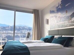 A hotel room with a large window, a bed, a chair, and a painting of a mountainous landscape. - Garda Hotel Forte Charme (Nago-Torbole)