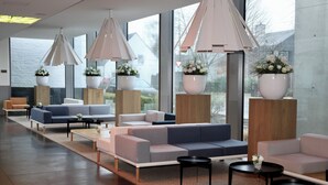 Un espace de détente moderne, doté de canapés, de tables et de grandes fenêtres offrant une vue sur l’extérieur.