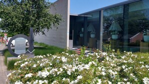 Un bâtiment moderne doté d’un espace d’accueil, entouré d’arbustes à fleurs blanches et d’un grand arbre.