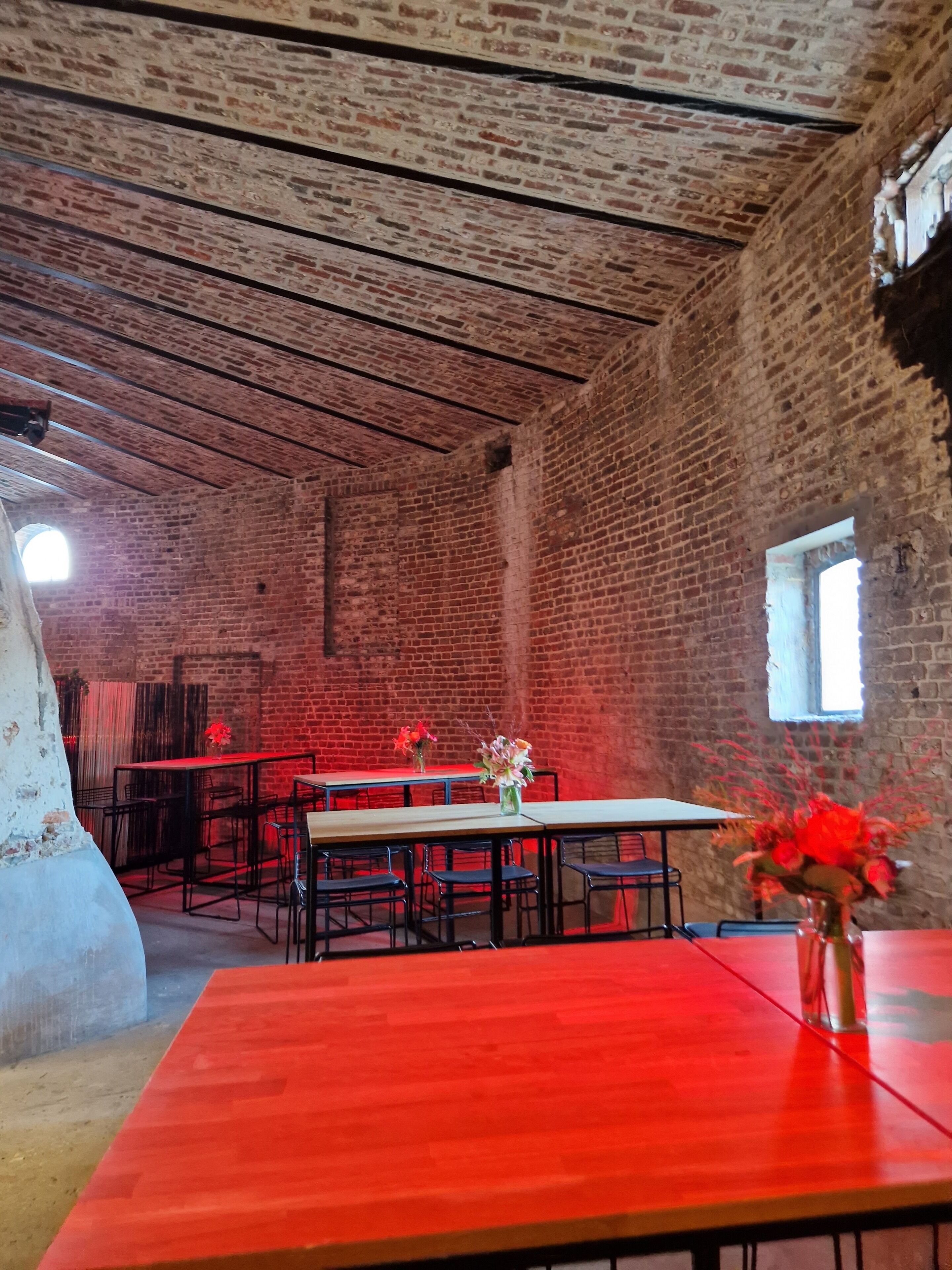 An interior with brick walls, exposed beams, and tables with chairs.