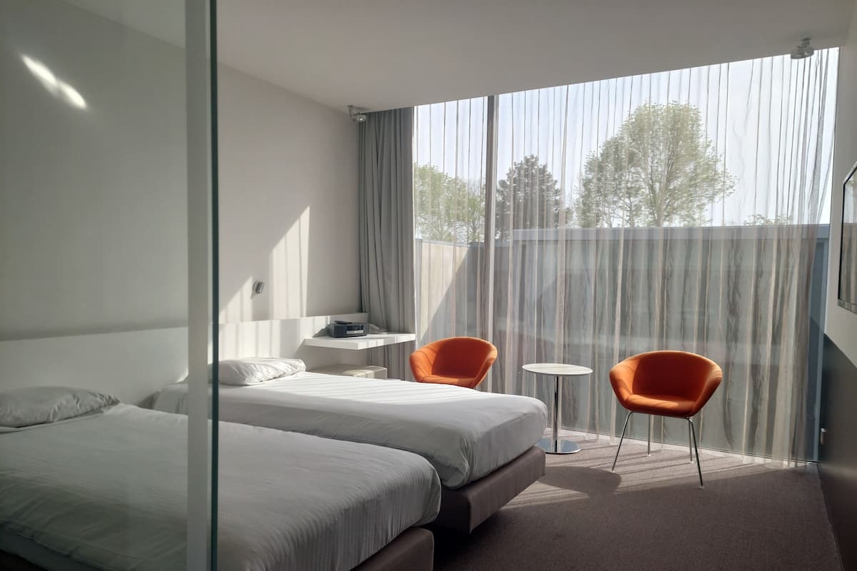 A hotel room with two beds, a small table, two chairs, and a large window with curtains.